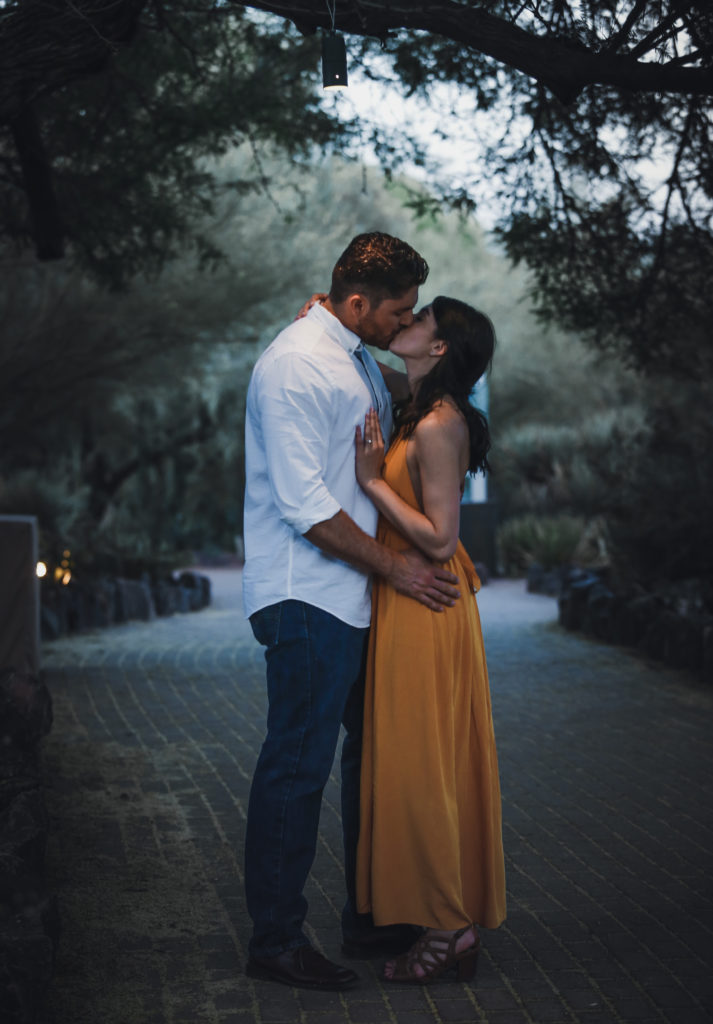 man and woman kiss under a small light hanging from a tree