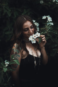 Model Cameo Rose at a photo shoot smelling a white flower. The image overall is dark aside from the flower petals and model.