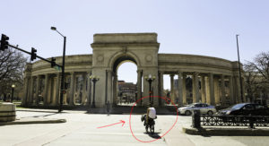 Man riding bike across crosswalk towards Denver's State Capitol Park.