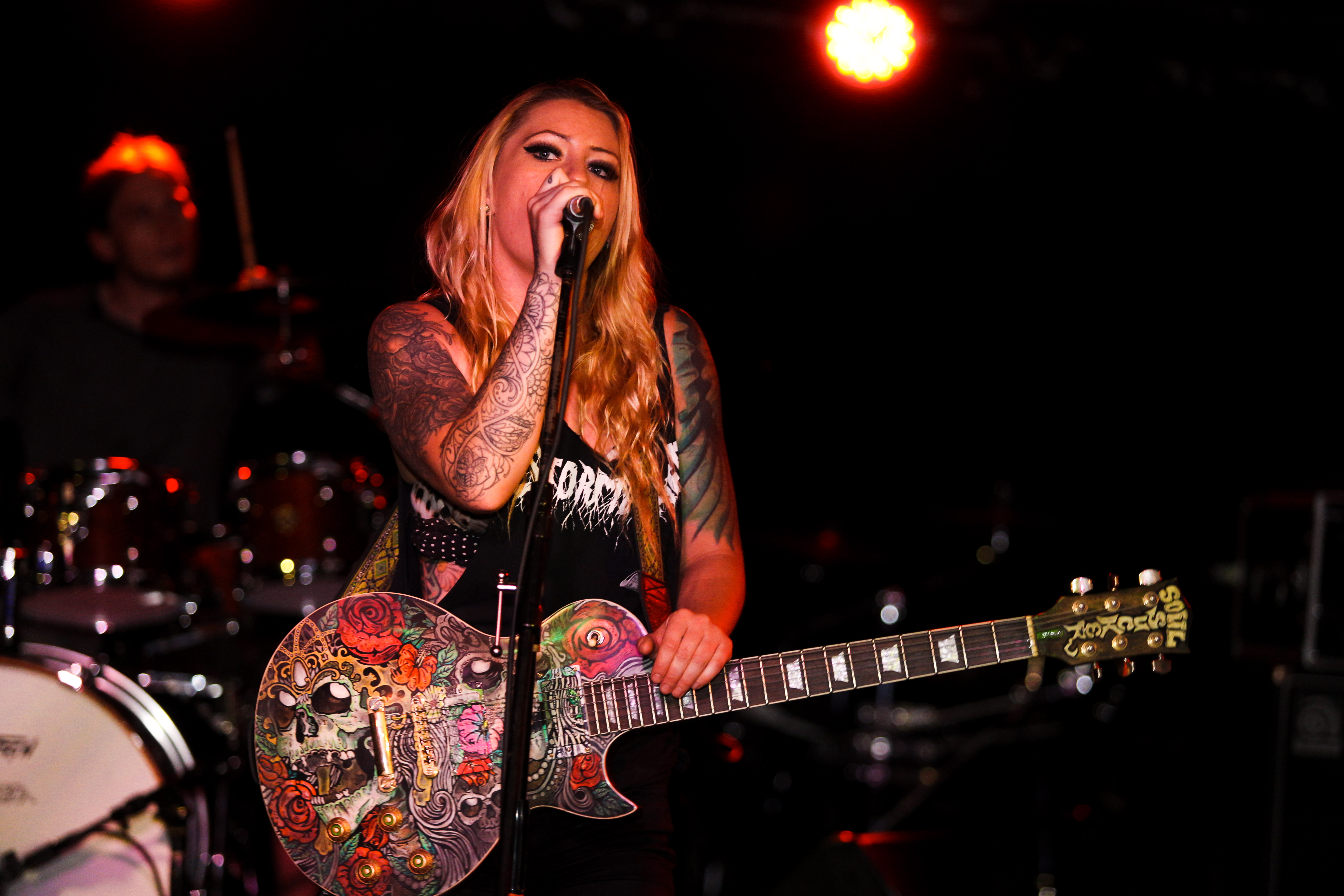 Female singer of Drozer singing with a beautiful guitar. The guitar is shiny with roses and skulls interlaced.