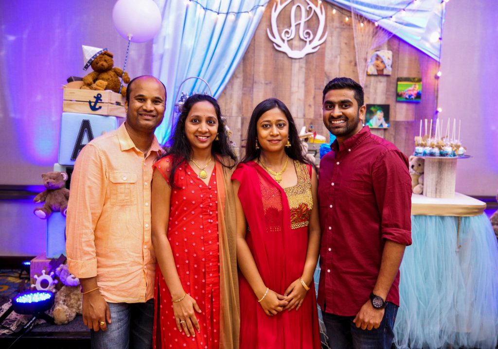 Two siblings and their spouses are posing together at a party. The subjects and the background are both well lit due to a good balance of ISO and flash.