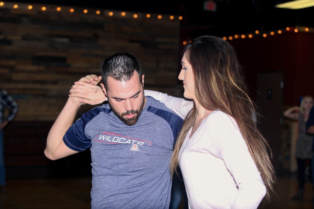 Two people dancing in a country bar. The dancers are very well lit in the image, but the background is very dark.